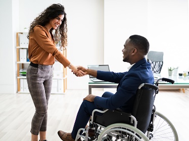 A woman shaking hands with a man in a wheelchair. 